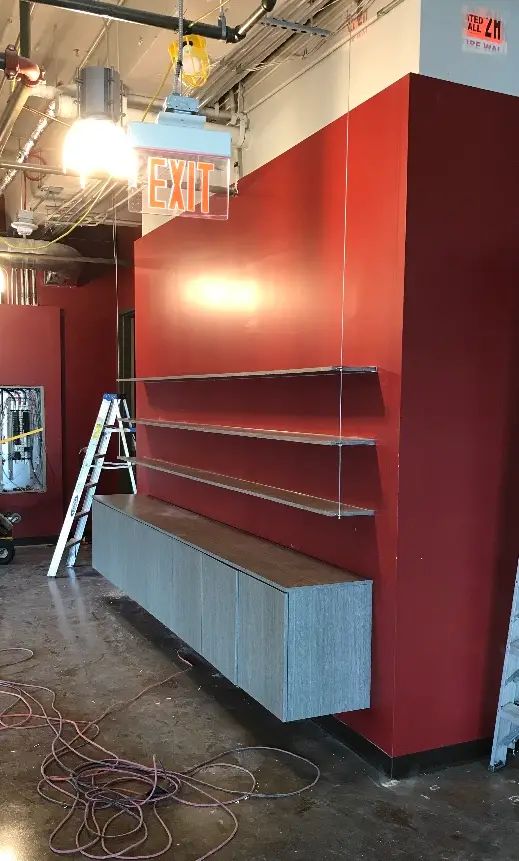 Retail display shelving and base cabinetry under construction against a red feature wall