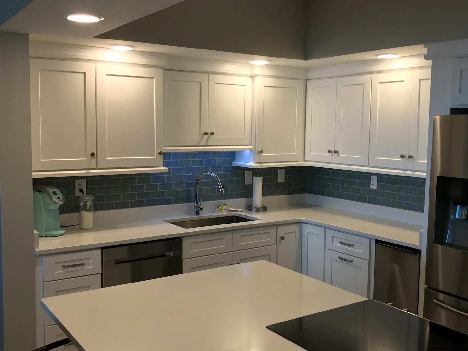 Finished kitchen with white cabinetry, a blue tile backsplash and dark countertops