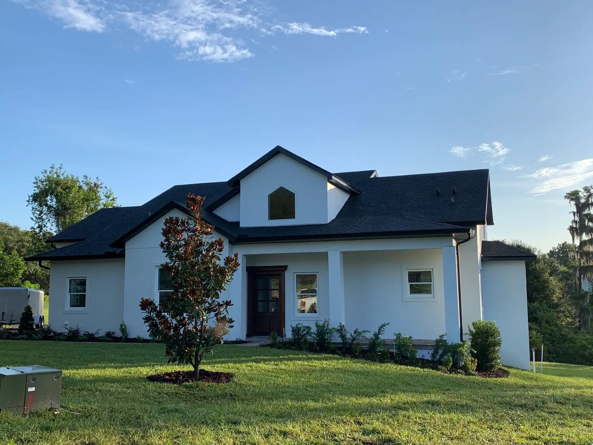 Completed new-construction home exterior with white siding, dark shutters and a covered porch
