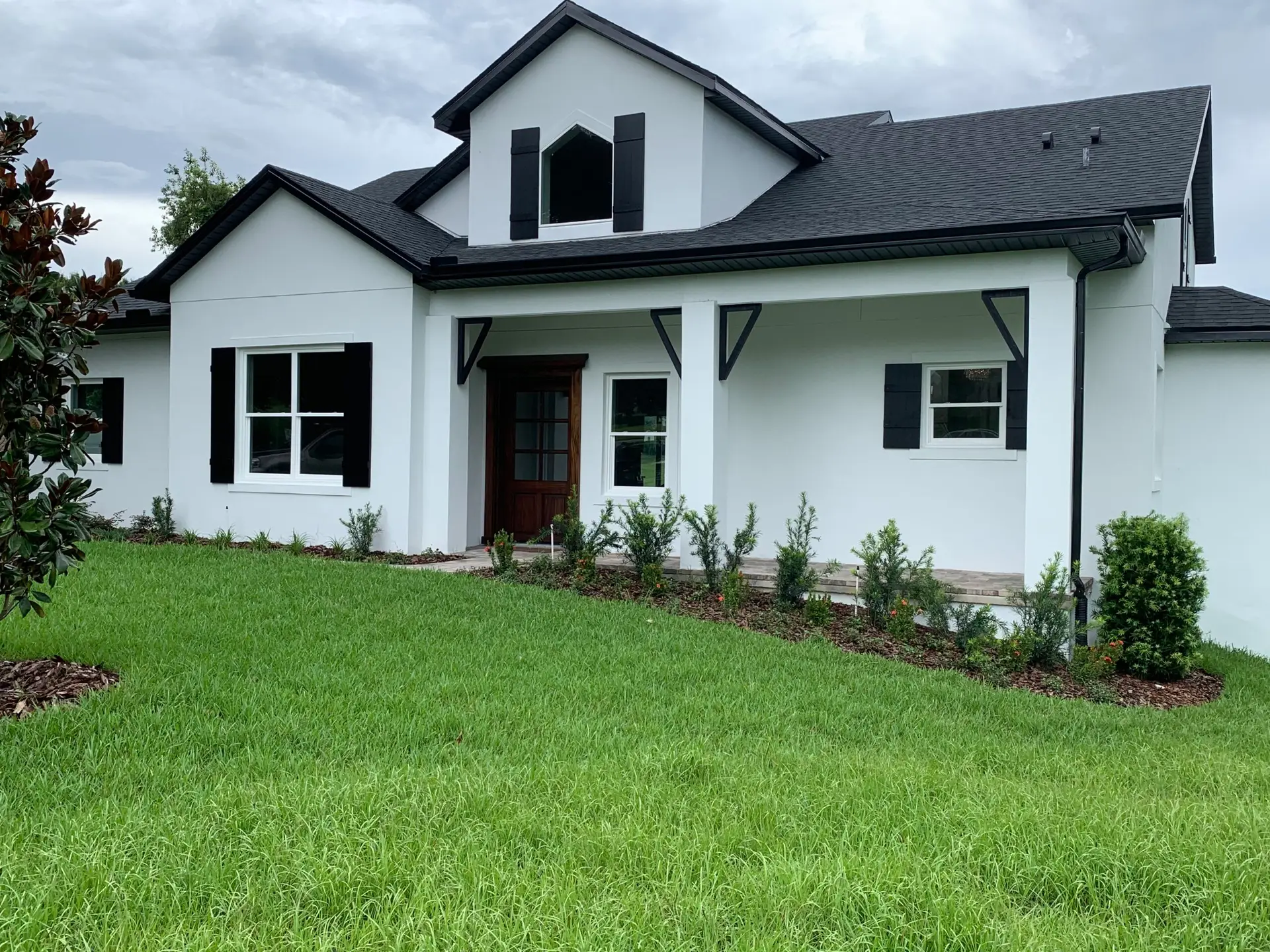 Completed home exterior with white siding, dark shutters and a gabled entry