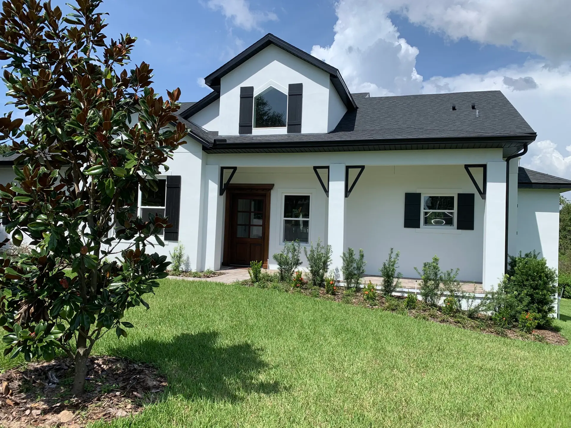 Completed home exterior with white siding, dark shutters and a covered entry porch