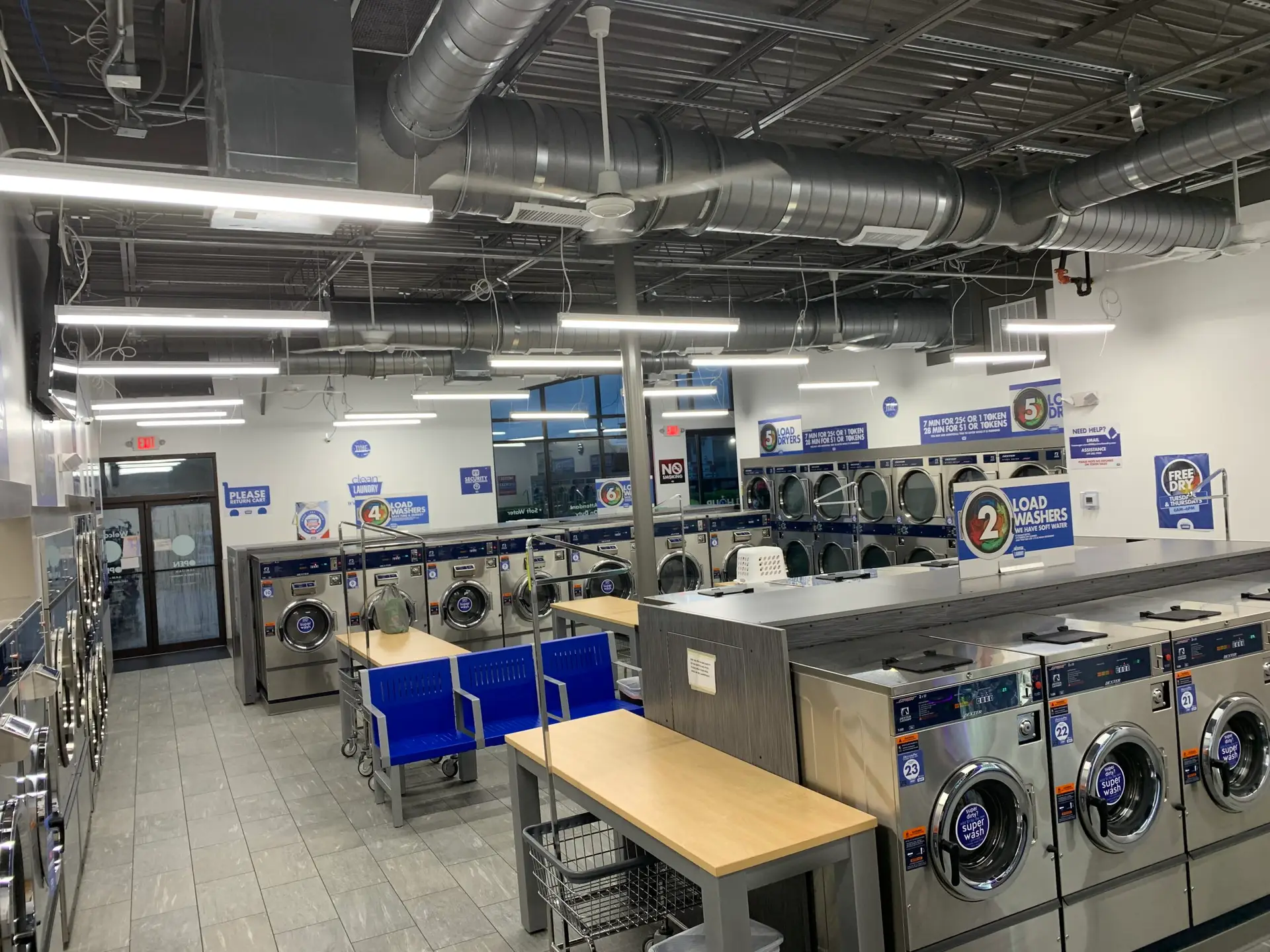 Finished laundromat tenant buildout with commercial washers, dryers and folding counters under an exposed ceiling