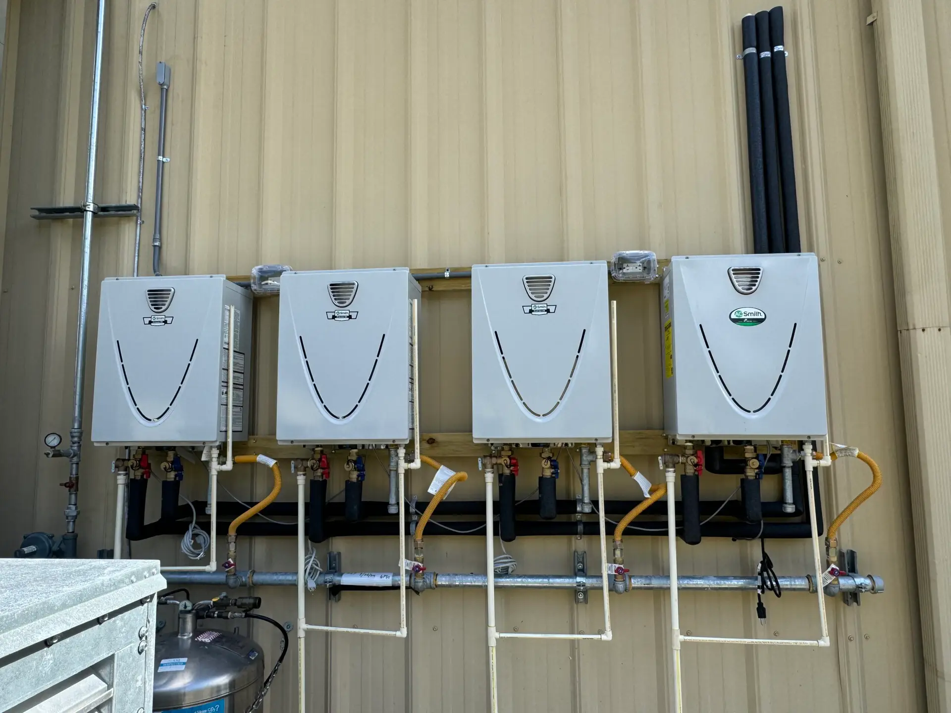 Bank of four wall-mounted tankless water heaters with manifolded gas and water piping