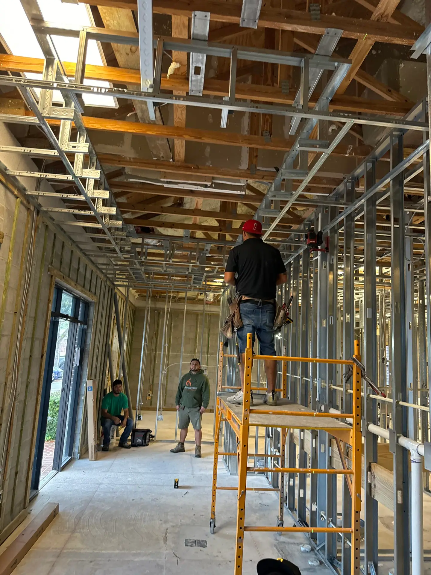 Interior framing and overhead rough-in underway with a carpenter working from a ladder